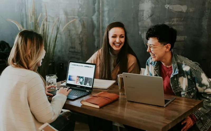 Estudantes reunidos em volta de uma mesa com notebooks.